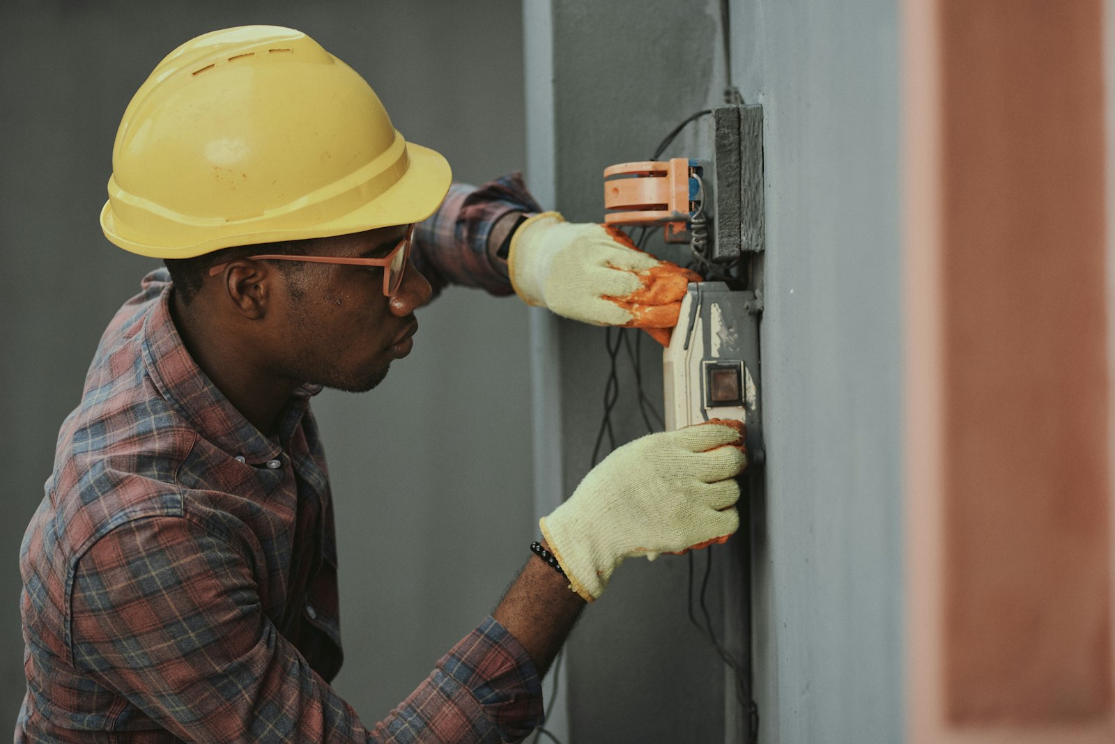 An electrician in a hard hat testing a wall socket with a meter